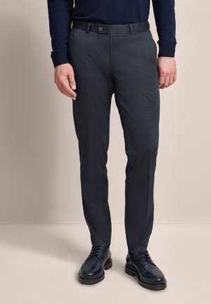 Dunkelgraue maßgeschneiderte Hose aus strukturiertem Stoff, mit Gürtelschlaufen, Knopfverschluss und leicht verjüngten Beinen, getragen mit dunklen Schuhen.