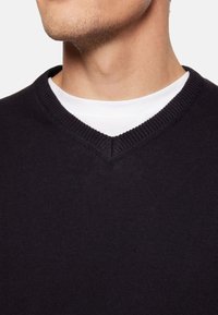 Pulover negru cu decolteu în V, cu guler cu nervuri și textură moale a materialului. Purtați peste un tricou alb cu guler rotund, vedere detaliată a părții superioare a corpului.