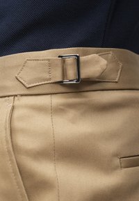 Παντελόνι χακί με λεία υφή, που διαθέτει ορθογώνια μεταλλική αγκράφα και ραμμένη μέση, σε συνδυασμό με μπλε ναυτικό τοπ με υφή.