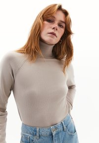 Turtleneck trui in lichtbeige, gemaakt van zachte stof. Beschikt over een geribbelde halslijn en raglanmouwen, gecombineerd met lichtblauwe high-waisted jeans.