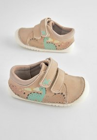 Chaussures en cuir beige avec une bande auto-agrippante, ornées d'un design de dinosaure vert pâle et d'une semelle texturée. Les accents incluent des coutures brunes.