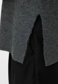 Ciemnoszary sweter z dzianiny o teksturowanym wykończeniu, z rozciętym dołem. Nosi się go na czarnym materiale, co podkreśla warstwowy styl.