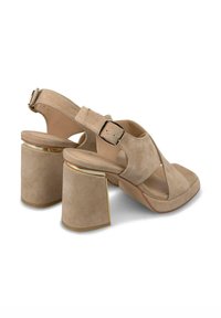 Sandales à talons hauts en suede beige avec un bout fermé, un dos ouvert et une bride ajustable à la cheville. Le talon bloc présente un accent doré.