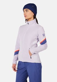 Giacca in pile di un leggero colore lavanda con colletto alto, chiusura con zip e tasche laterali. Accentuata da strisce blu e arancioni sulle maniche.