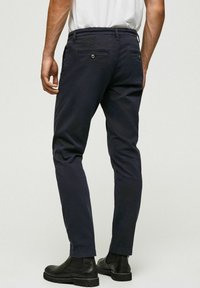 Tmavě modré kalhoty vyrobené z bavlny s úzkým střihem. Mají dvě zadní kapsy a jemné detaily prošití. Noseny s černými chelsea botami.