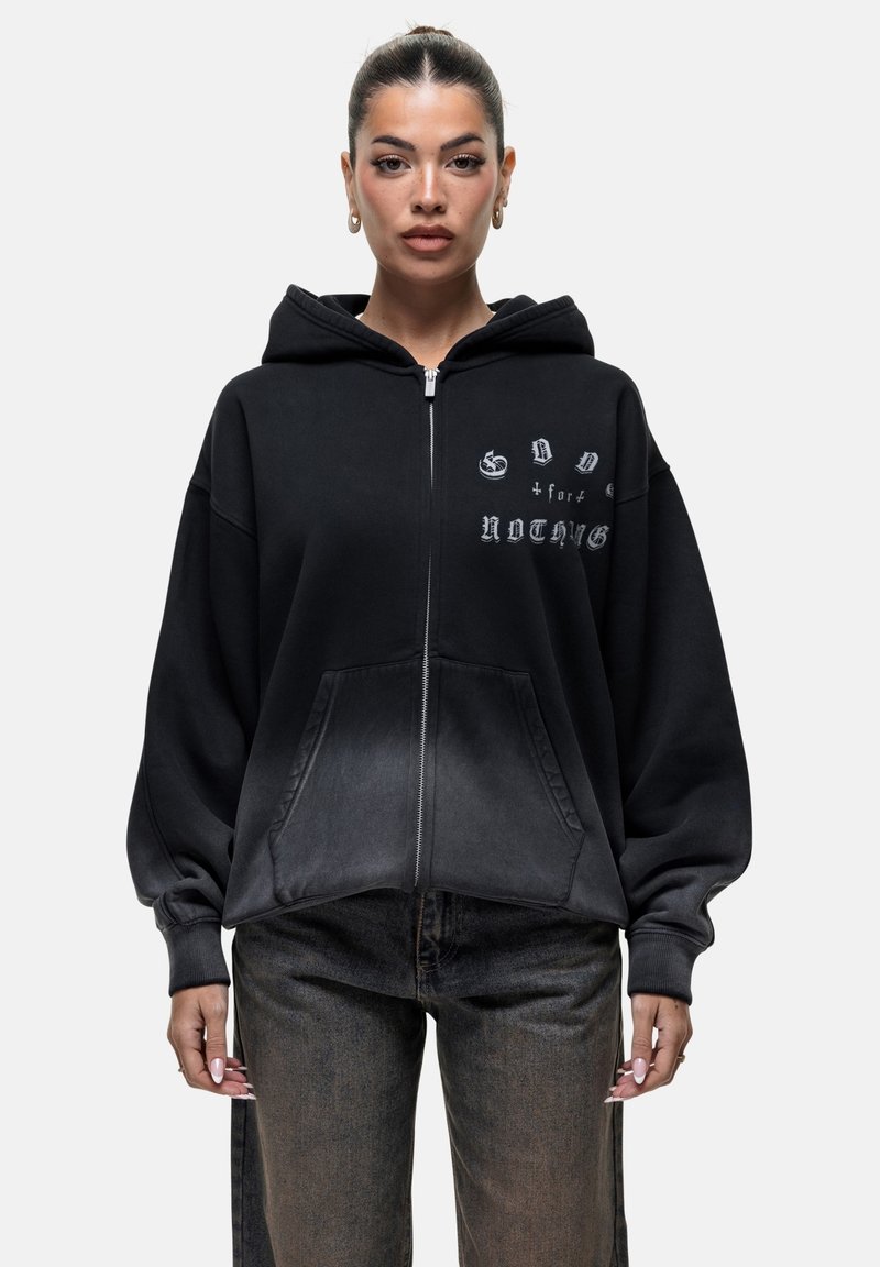 Felpa nera con zip, dalla texture leggermente sbiadita, fit oversize e testo grafico frontale. Presenta un ampio cappuccio e tasche anteriori.