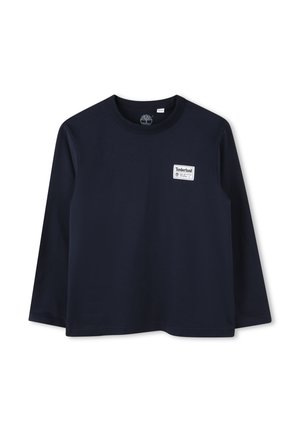 T-shirt à manches longues bleu marine en coton avec un col rond. Présente un patch logo Timberland blanc sur la poitrine gauche. Texture lisse.