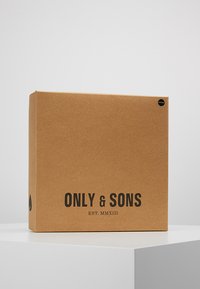 Firkantet kraftpapiræske med sort tekst "ONLY & SONS" og "EST. MMXIII" samt et rundt sort klistermærke i øverste højre hjørne.