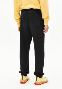 Zwarte joggingbroek met een achterzak, een elastische tailleband en geribbelde boorden. Draagt gele en oranje sneakers met een gestructureerd ontwerp.