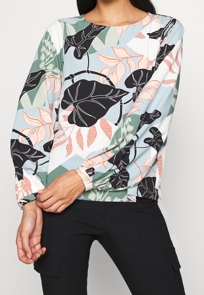 Camicia a maniche lunghe con motivo floreale in azzurro chiaro, caratterizzata da foglie nere e fiori pesco. Tessuto morbido con una vestibilità rilassata e maniche arricciate.