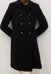 Abrigo de lana negro con diseño de doble botonadura, con botones plateados, cuello y bolsillos laterales. Textura suave y corte hasta la rodilla.