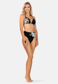 Czarny zestaw bikini z trójkątnym topem i wysokim stanem, ozdobiony białymi printami róż. Gładka tekstura materiału, minimalistyczny design.