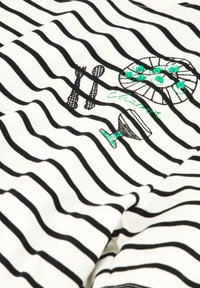 Witte stof met zwarte strepen heeft kleurrijke geborduurde ontwerpen van bestek en een cocktailglas, wat textuur en detail toevoegt.