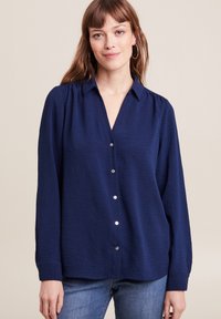 Navyblauwe blouse met knoopjes, gemaakt van textuurstof, met een kraag en lange mouwen met subtiele geplooide details.