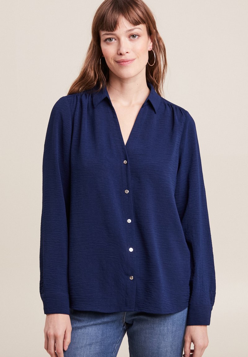 Navyblauwe blouse met knoopjes, gemaakt van textuurstof, met een kraag en lange mouwen met subtiele geplooide details.