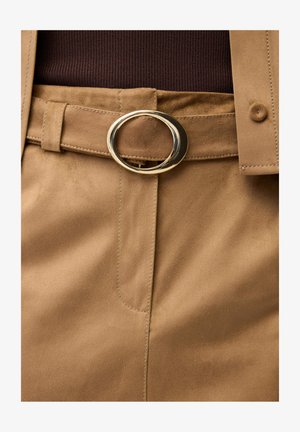 Tan suede high-waist pants with a matching belt fastened by a shiny gold oval buckle over a dark brown top.