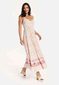 Maxi dress in light pink with floral pattern. Features thin straps, gathered bodice, and tiered skirt with decorative border. Designed for summer wear.
