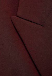 Burgundin kangas, jossa on sileä pinta ja muotoiltu läppä siistillä ompeluyksityiskohdalla, korostaen ryhdikästä muotoilua.