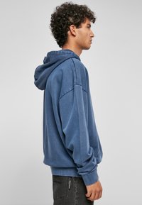 Felpa con cappuccio blu dal taglio rilassato, con polsini a costine e tessuto morbido al tatto. Presenta un cappuccio ampio e cuciture sulle spalle abbassate.