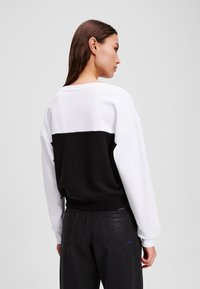 Felpa con collo rotondo, caratterizzata da una parte superiore bianca e una parte inferiore nera. Realizzata in tessuto morbido, con una vestibilità comoda e polsini a coste.