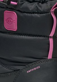 Bota impermeable negra con superficie texturizada, detalles en rosa y parche con el logo de Geox. Cordones y costuras visibles a lo largo del diseño.