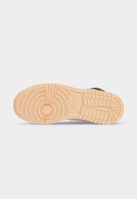 Σόλα σε μπεζ αθλητικό παπούτσι Nike με κυκλικά μοτίβα, βαθιά αυλάκια και το λογότυπο Nike εγχαραγμένο κοντά στη μέση.