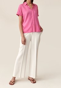 Rosa kurzärmliges Hemd mit Knöpfen, lockere Passform, kombiniert mit weißen weit geschnittenen Hosen und braunen Flip-Flops. Glatter Stoff, minimalistisches Design.
