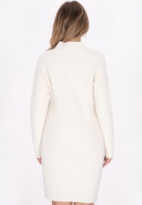 Abito in maglia a coste di colore crema con collo alto e maniche lunghe, caratterizzato da una vestibilità morbida e orlo a ginocchio. Texture morbida e design minimal.
