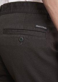 Close-up of dark trousers back pocket with button and small "Marc O'Polo" brand label above pocket.