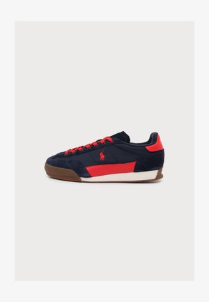Baskets bleu marine avec des accents rouges, des lacets rouges, une semelle marron et un logo polo rouge sur le côté, présentées sur fond blanc uni.