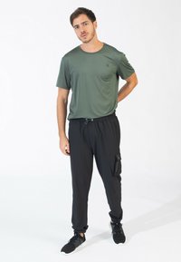 Groen gestreepte sport T-shirt, zwarte cargobroek met zijzak, en zwarte sneakers. Comfortabele pasvorm en lichtgewicht stof.