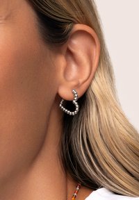 Pendientes de aro plateados con un diseño de cuentas, que presentan una forma ondulada y una textura pulida, exhibidos en una oreja.