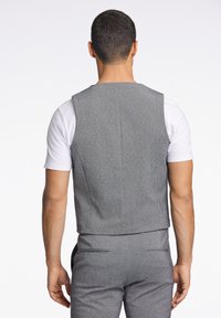 Grå ärmlös väst tillverkad av texturerat tyg, med en figursydd design. Den har en ren bakseam och är ihopparad med en vit T-shirt.