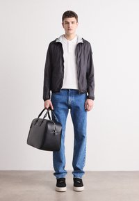Geacă ușoară neagră cu fermoar și căptușeală gri, tricou polo alb, blugi albaștri, geantă de piele neagră și adidași negri cu talpă albă.