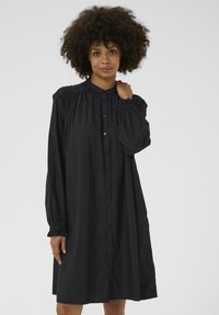 Robe noire à boutons, faite d'un tissu doux, avec un design de manche froncée, des manches bouffantes longues et une coupe décontractée.