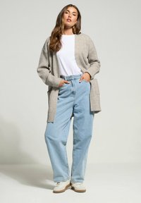 Cardigan grigio chiaro a costine abbinato a una camicia bianca e jeans leggeri azzurri a gamba larga, con tasche laterali e sneakers bianche.