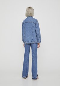 Denimjacketing en uitlopende spijkerbroek in lichtblauw, met een relaxte pasvorm, zichtbare stiksels en zijsplitten aan de zoom van de broek.