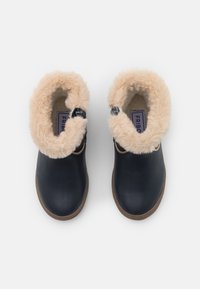 Botas de tobillo de cuero azul oscuro con un suave collar y forro interior de piel sintética beige, que cuentan con un cierre lateral de broche y suela de goma marrón.