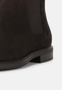 Μποτάκι αστραγάλου από μαύρο σουέντ με λεία υφή, ελαστική πλαϊνή πλευρά και χοντρό τακούνι με επίπεδη βάση.