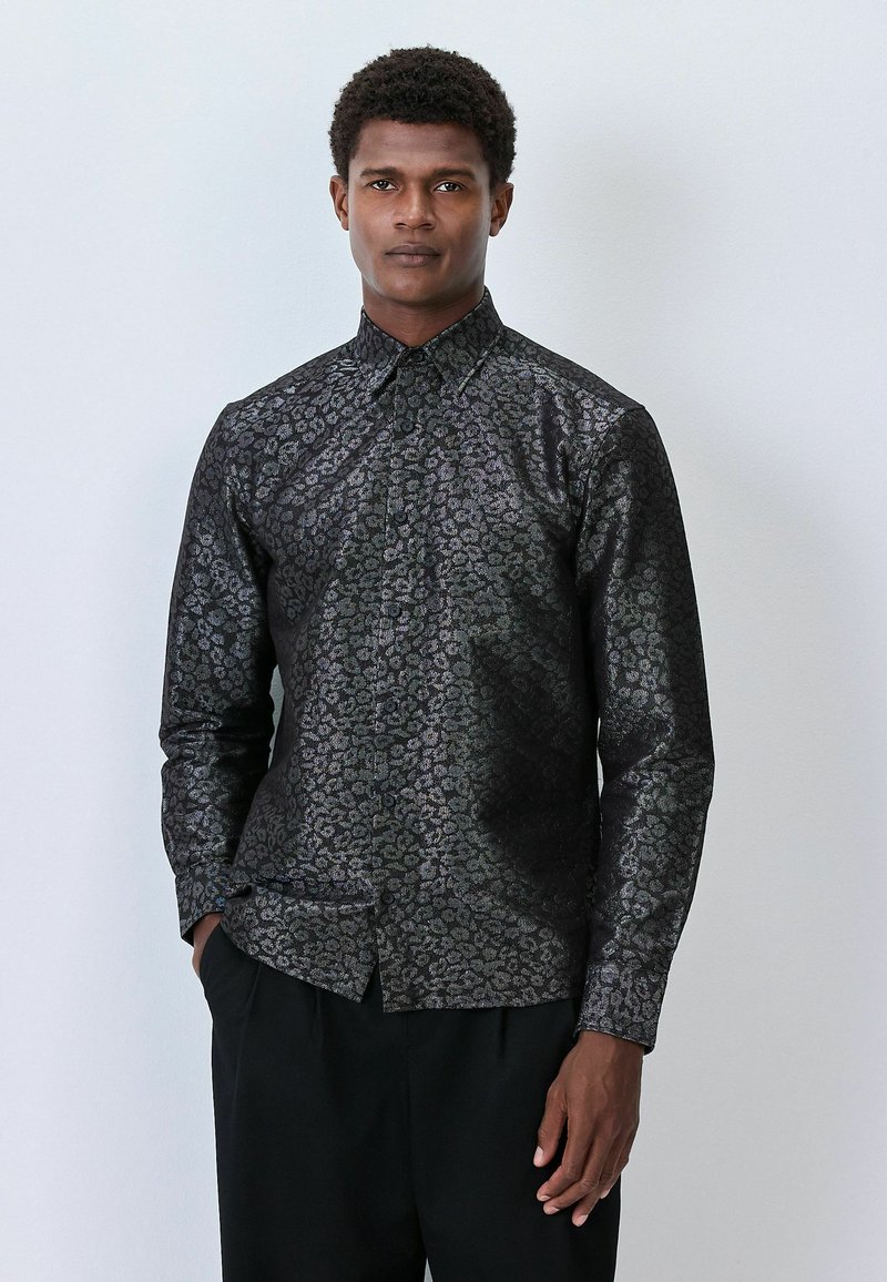 Czarna koszula w panterkę o błyszczącej fakturze, z długimi rękawami, kołnierzykiem zapinanym na guziki i dopasowanym krojem, w połączeniu z ciemnymi spodniami.