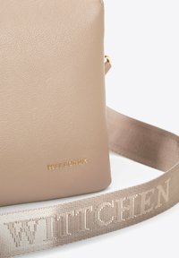 Borsa a tracolla beige realizzata in materiale testurizzato, con un logo dorato e una tracolla in tessuto con motivo in una tonalità coordinata.