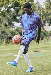 Puma soccer kit featuring a blue and purple geometric pattern, paired with white socks and colorful soccer cleats. Standard field background.