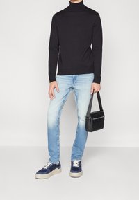 Svart polotröja, ljusblå jeans, marinblå och vita sneakers samt en svart crossbody-väska. Fokusera på en avslappnad passform och texturer.