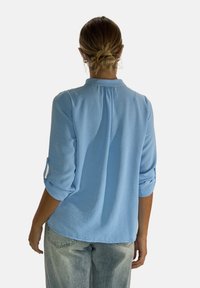 Jasnoniebieska koszula z kołnierzykiem, długimi zrolowanymi rękawami i teksturowanym materiałem. Tył z delikatnym detalem yoku.