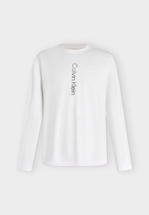 Camiseta blanca de manga larga con cuello redondo con el logo "Calvin Klein" impreso verticalmente en negro en el centro delantero.