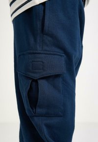Marineblaue Cargo-Hose mit weichem Material, ausgestattet mit einer seitlichen Tasche mit Klappe, gestickten Akzenten und einer bequemen Passform.