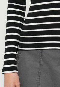 Arm and side torso wearing a black and white striped long-sleeve shirt over gray pants with visible stitching and pocket.