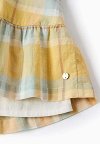 Top a maniche corte in plaid dai colori pastello (giallo, blu, pesca), realizzato in tessuto testurizzato con orlo a balza e un piccolo dettaglio con bottone.