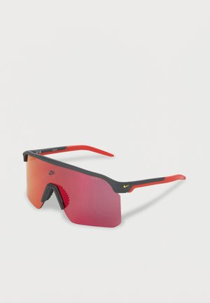 Sporty wraparound-solbriller med røde speilglass, svart og rød innfatning, og små gule Nike-logoer på linsen og på sidestroppene.
