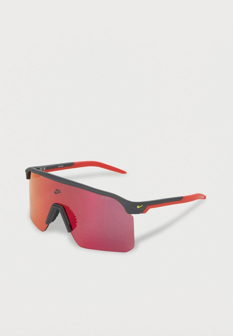 Αθλητικά γυαλιά ηλίου τύπου wraparound με κόκκινους καθρεφτιστούς φακούς, μαύρο και κόκκινο σκελετό και μικρά κίτρινα λογότυπα Nike στον φακό και στα κέρατα.